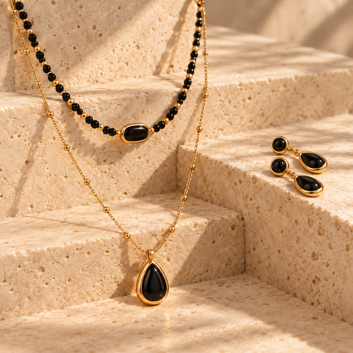 Jewelry Sets collection image featuring a black pendant necklace and matching black earrings styled on warm stone steps