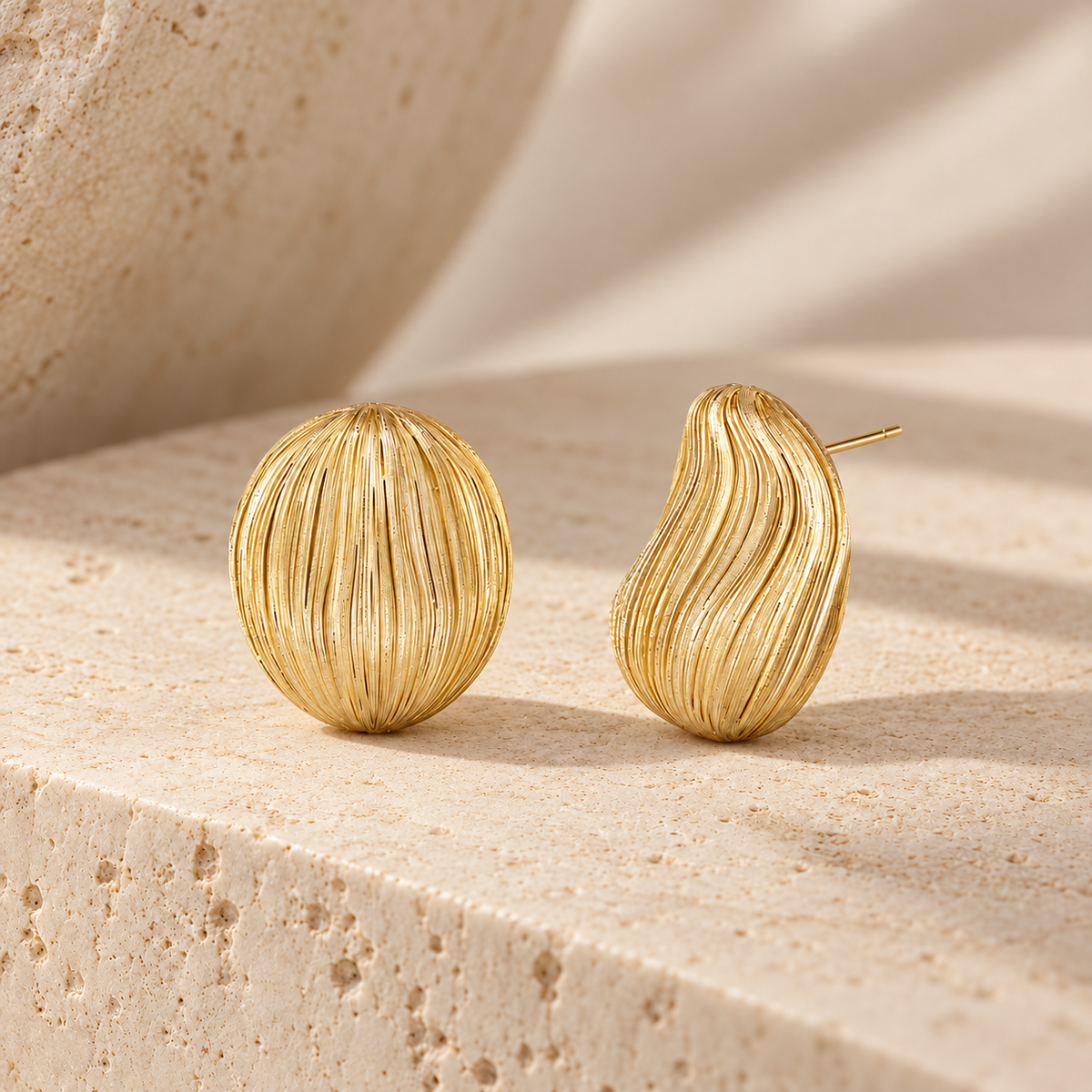 Gold-tone textured sculptural stud earrings on warm stone