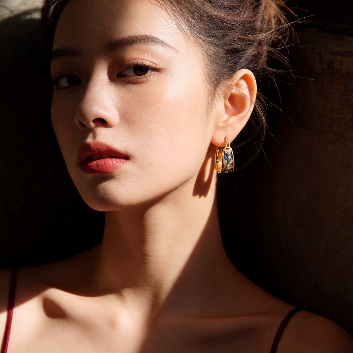 Model wearing gold-tone U-hoop earrings with abalone shell inlay