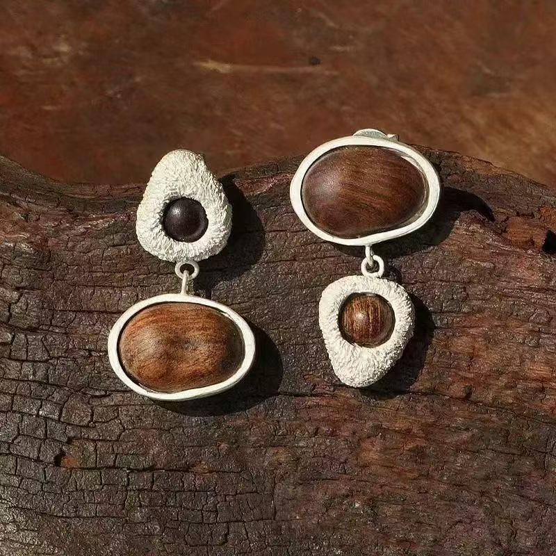 Asymmetric wood stud earrings displayed on natural wood
