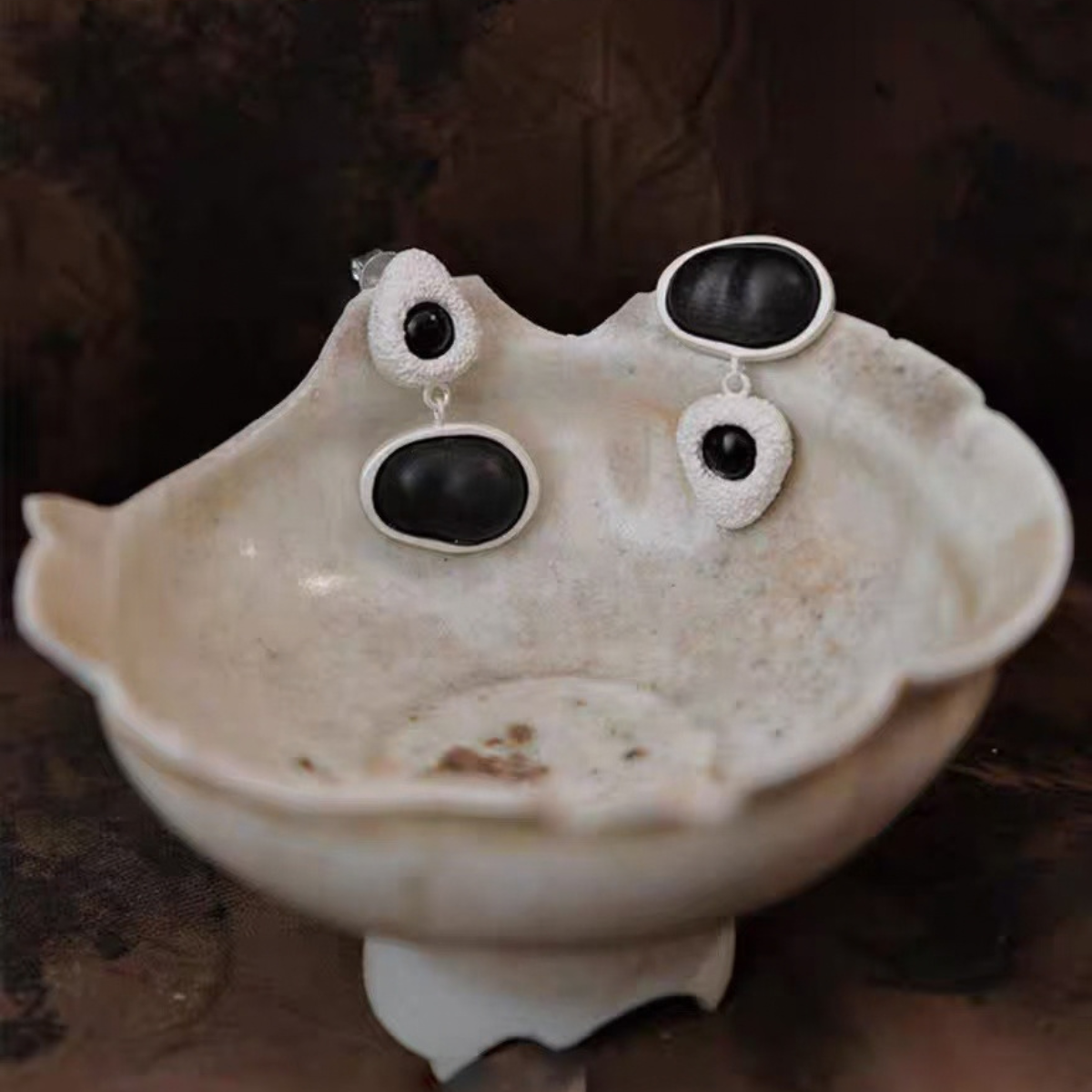 Asymmetric wood stud earrings displayed on ceramic
