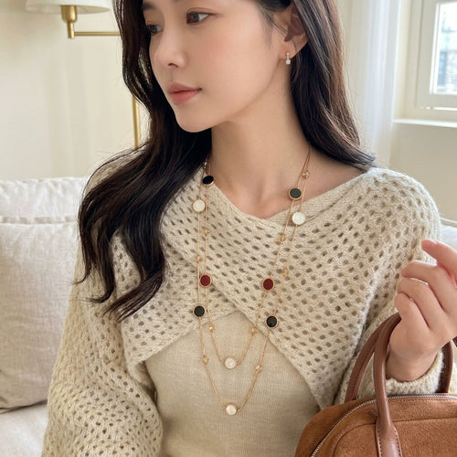 Model wearing a layered gold-tone necklace with black burgundy and pale accents