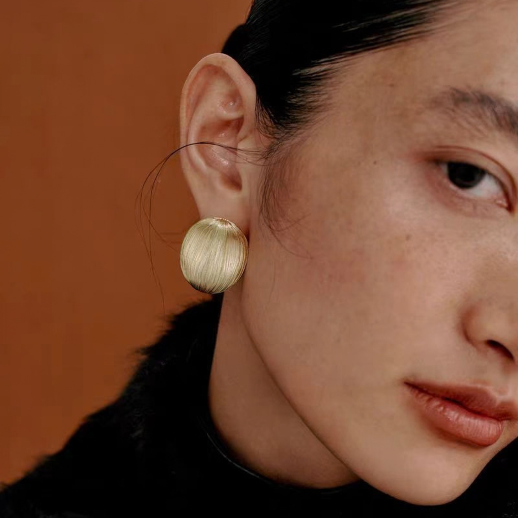 Model wearing Bound Light brushed sculptural stud earrings in Large Gold-Tone