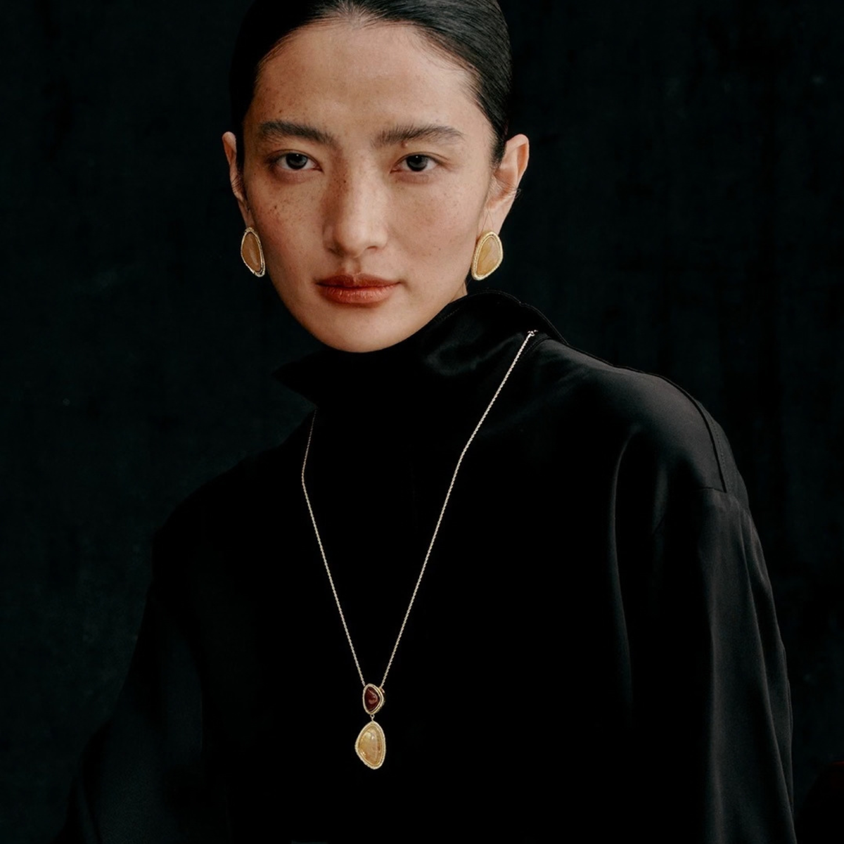 Model wearing the Gold-Tone Bound Light long natural stone necklace and triangle earrings