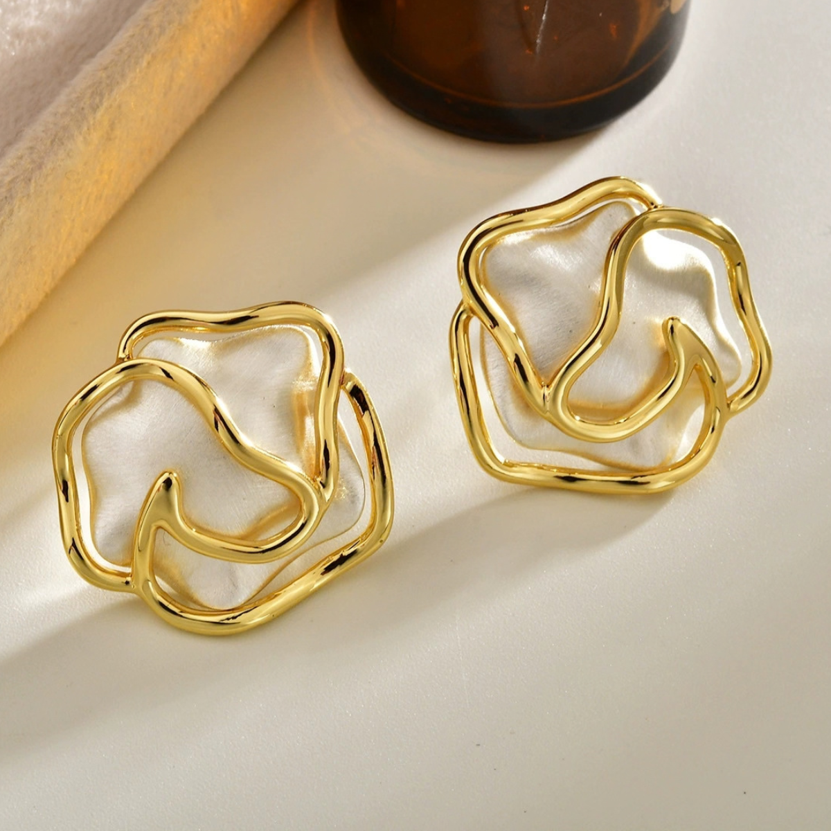 Close-up of brushed silver-tone rose stud earrings with flowing polished metal contours