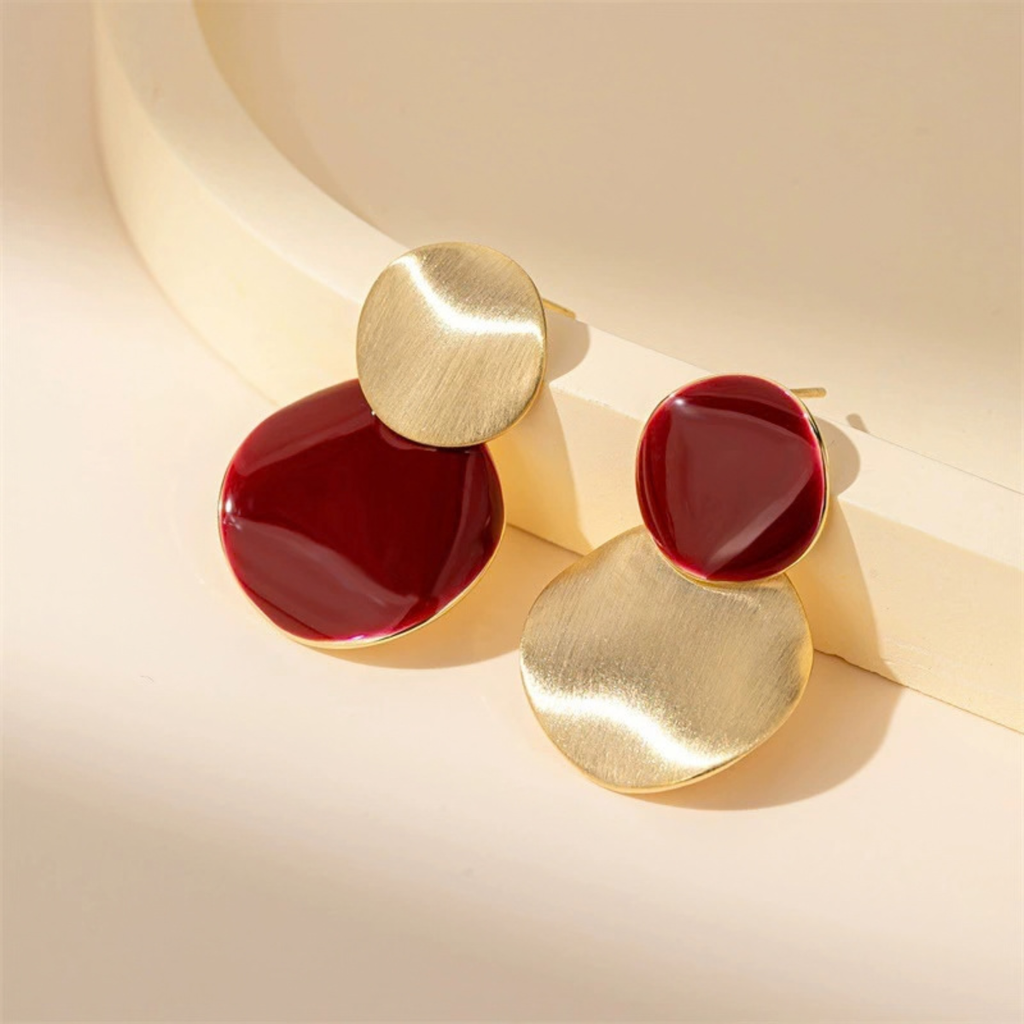 Close-up of asymmetric burgundy and brushed gold-tone stud earrings