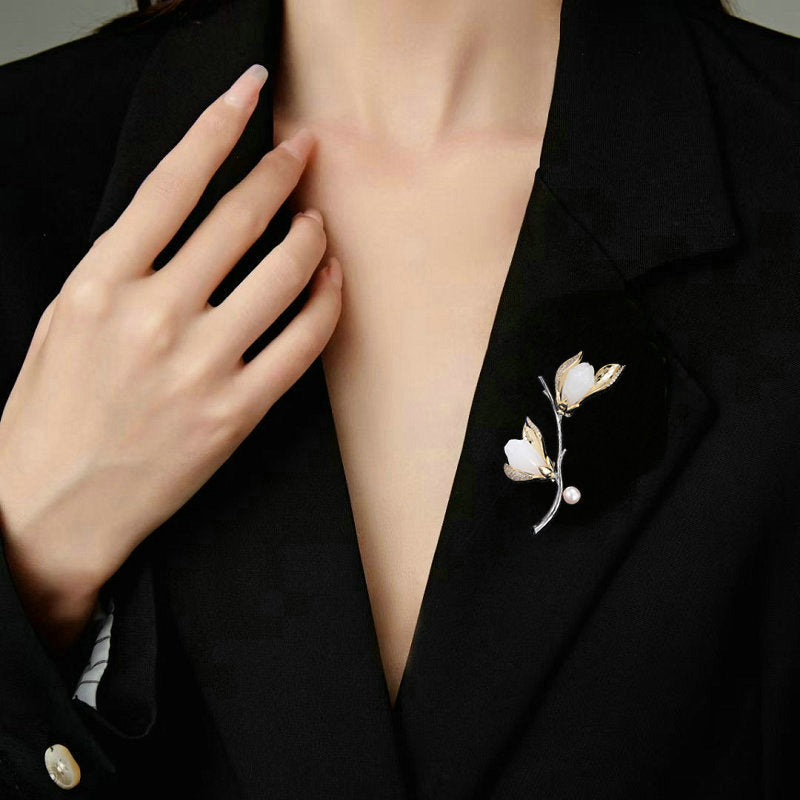 Gold-tone magnolia pearl branch brooch styled on a black blazer