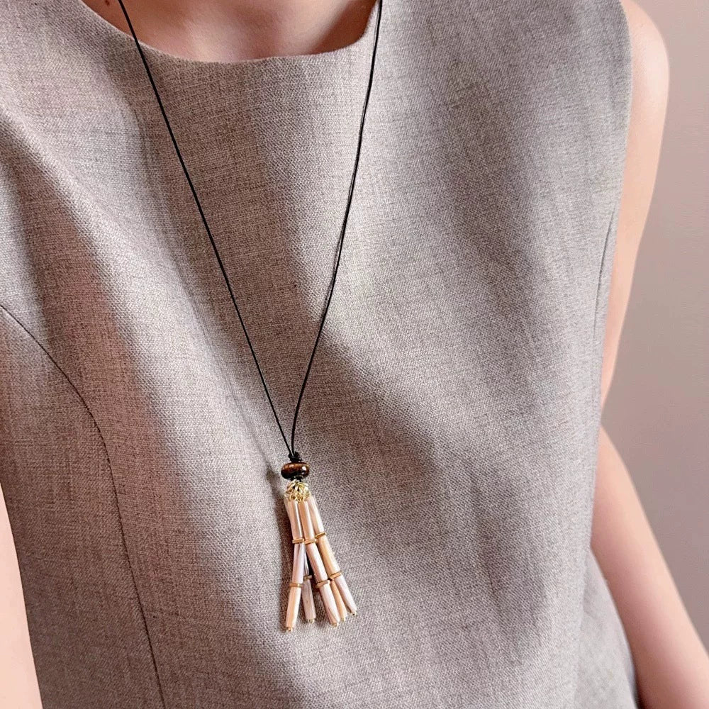 Mother-of-pearl tassel cord necklace worn long over a neutral top