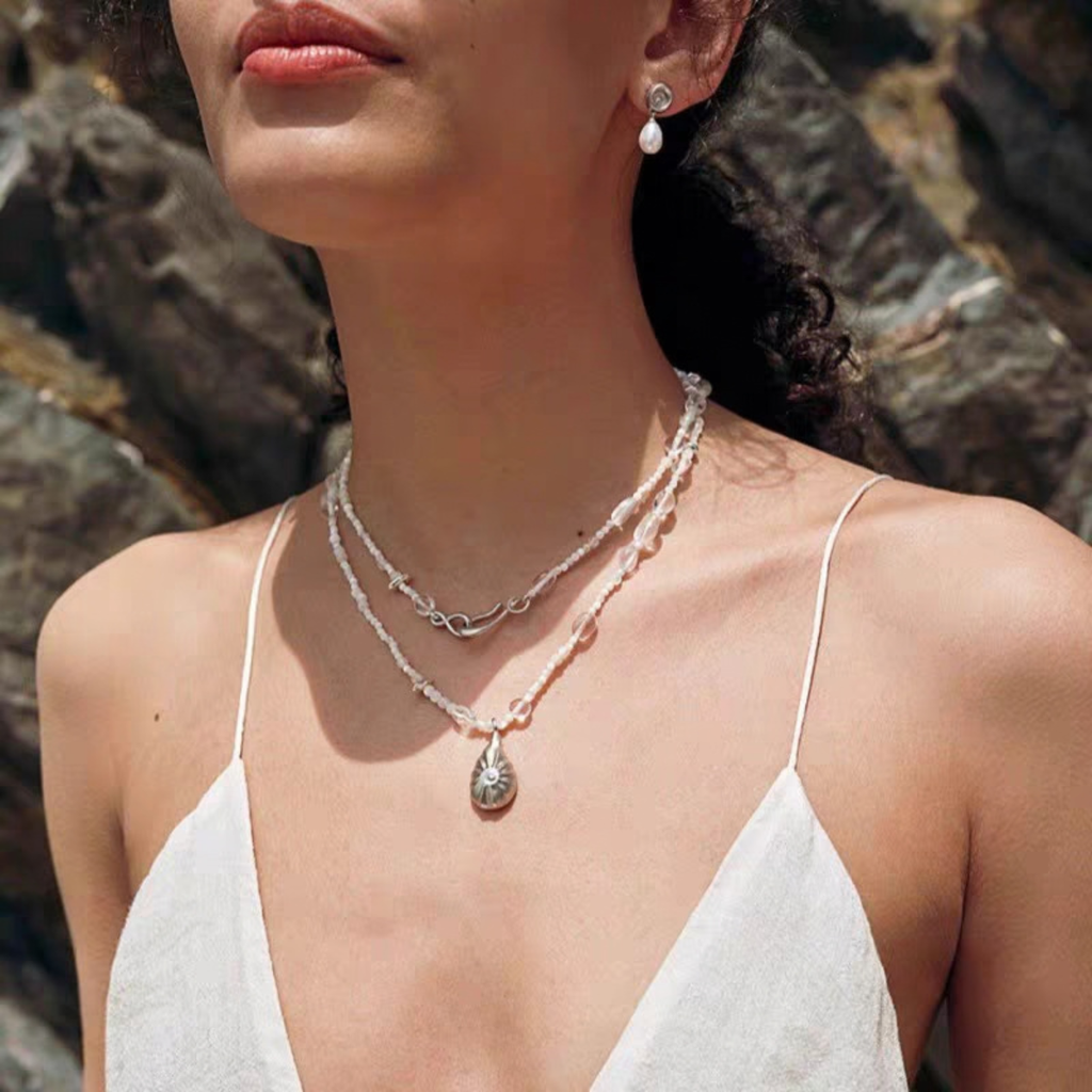 Long shell and crystal necklace featuring irregular beads and a sculptural silver-tone pendant