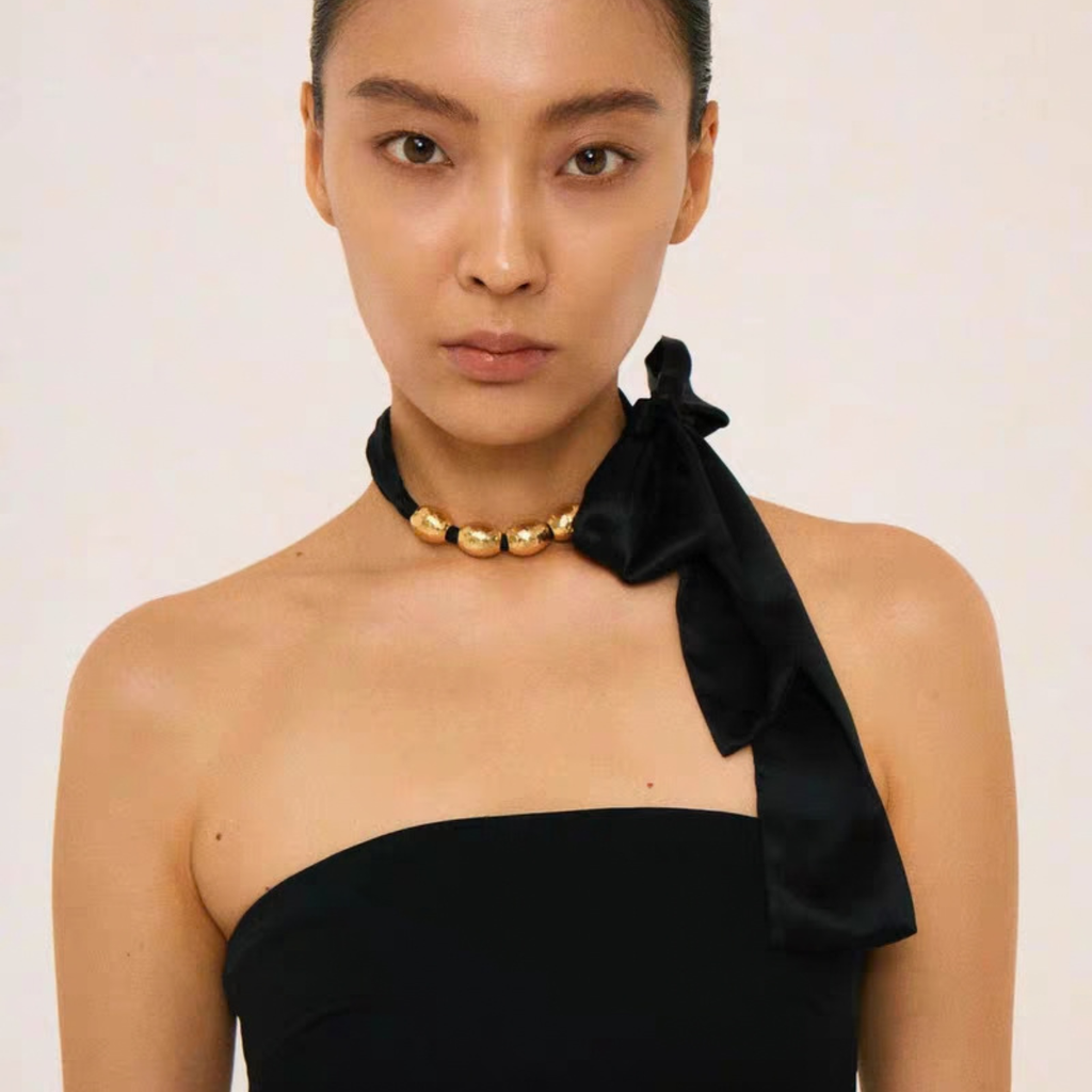 Sculptural gold bead ribbon necklace worn as a black choker