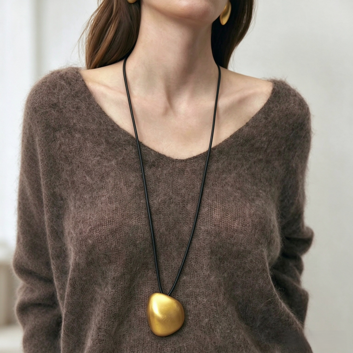 Model wearing a long gold-tone pebble pendant necklace over a brown knit top