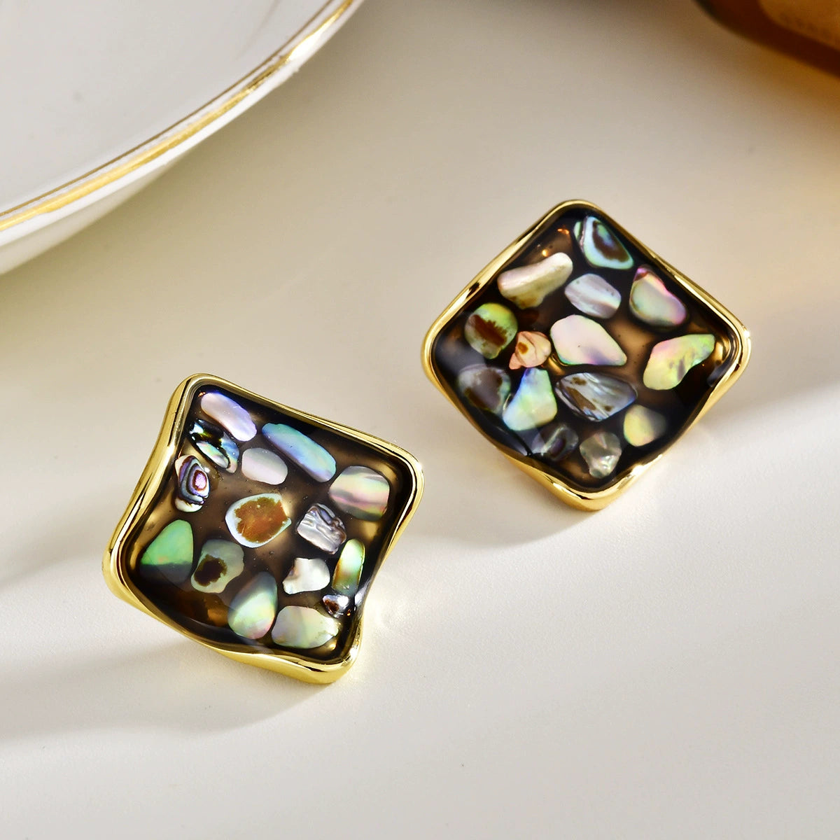 Close-up of black-back abalone square stud earrings with natural iridescent shell fragments