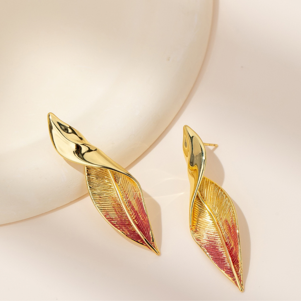 Close-up of gold-tone textured leaf stud earrings with red accents