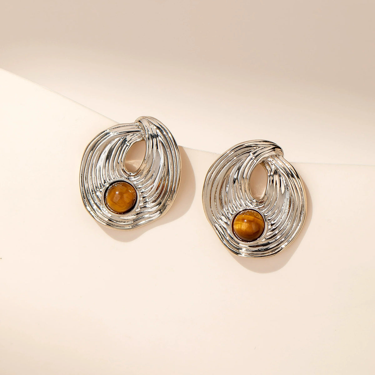 Close-up of silver-tone sculptural stud earrings with tiger eye stone