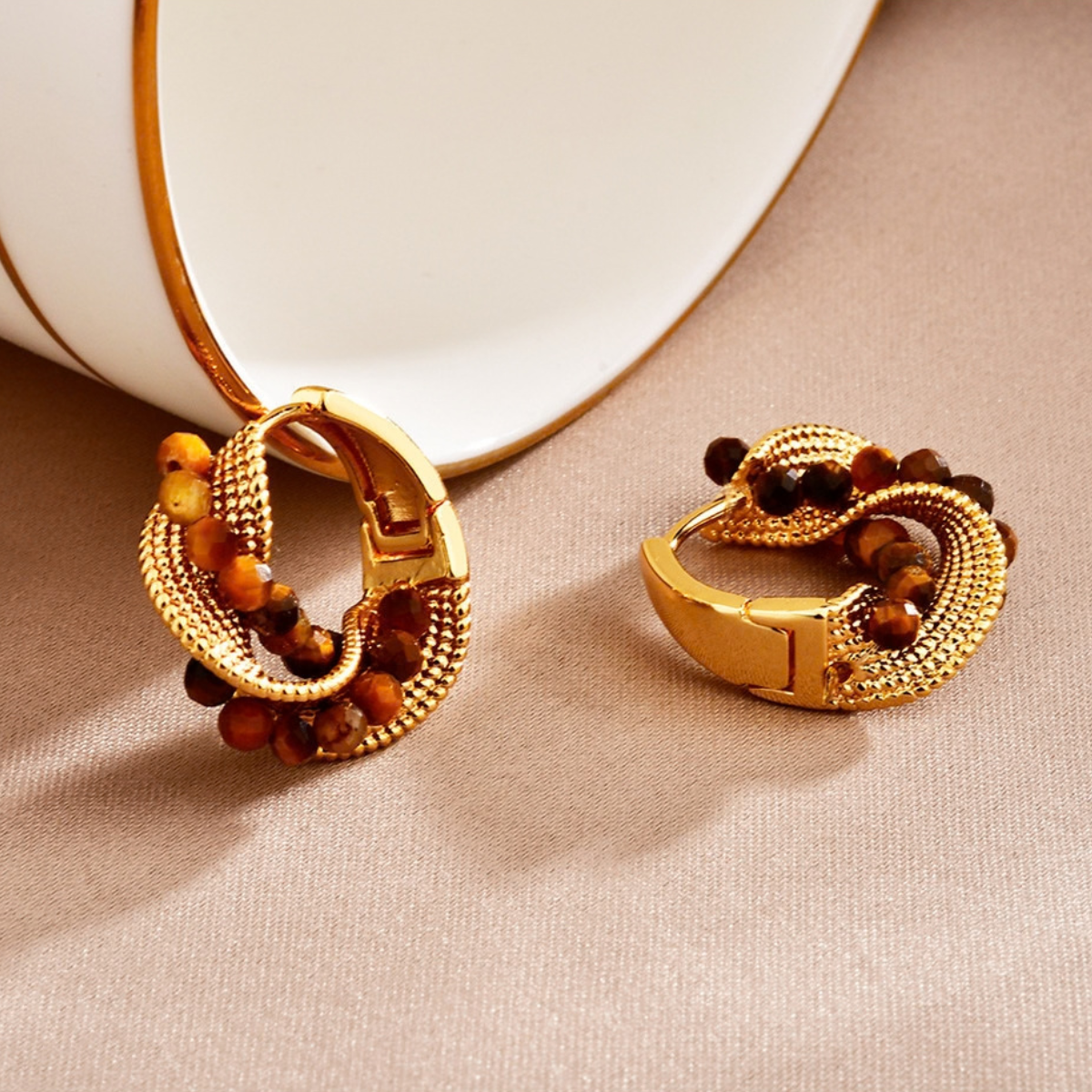 Twisted gold-tone hoop earrings with tiger eye beads on neutral fabric